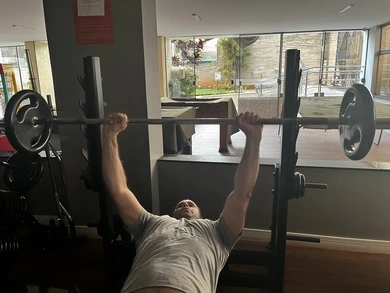 Uma pessoa deitada e erguendo uma barra com peso traz ganho de massa muscular