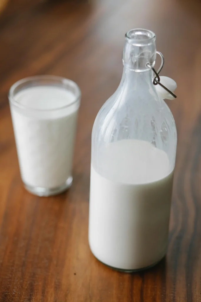 Uma garrafa de vidro com leite ao lado de um copo de vidro com leite. veja os benefícios do whey protein.