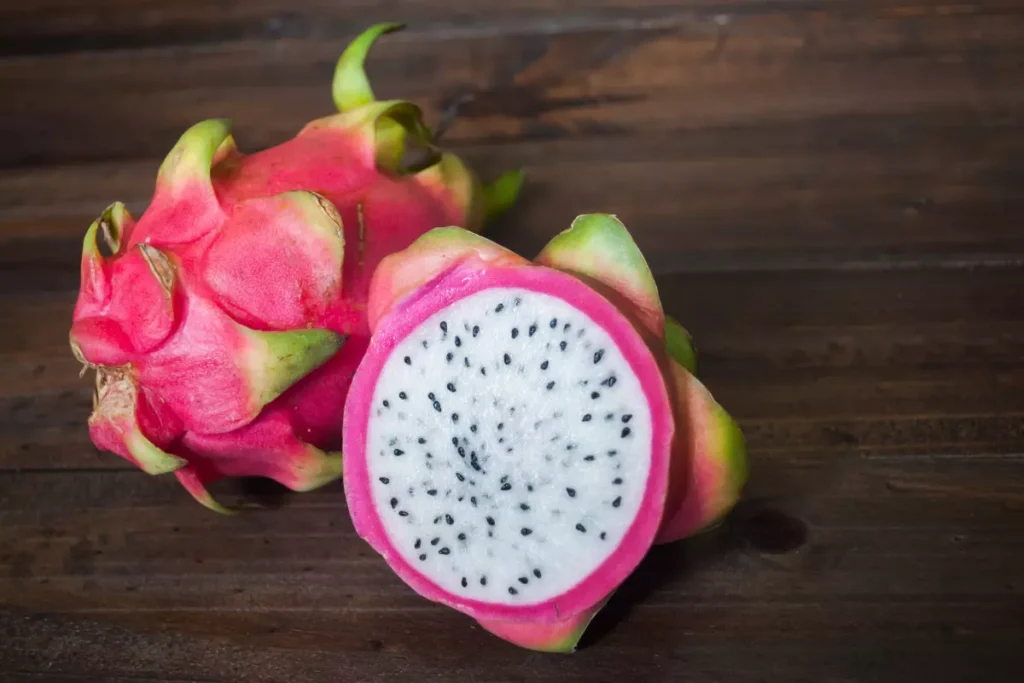 Uma pitaya partida pela metade ao lado de uma pitaya inteira. Elas estão entre as melhores frutas para emagrecer.