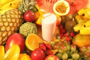 Uma foto de frutas como maça, abacaxi, laranja e maracujá com um copo de suco no meio. Descubra as melhores frutas para emagrecer
